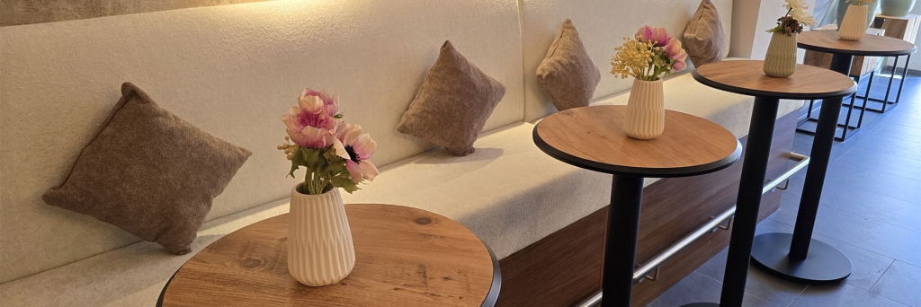 Moderne Lounge-Ecke mit bequemer Sitzbank, dekorativen Kissen und runden Holztischen.