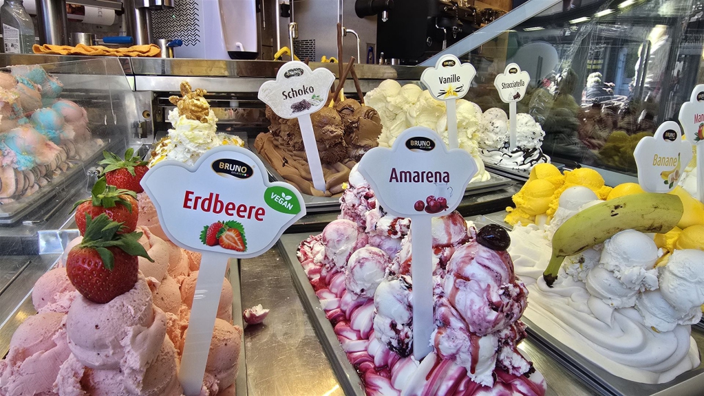 Eine reichhaltige und bunte Auslage von Gelato und Desserts in einer professionellen Kühlvitrine.