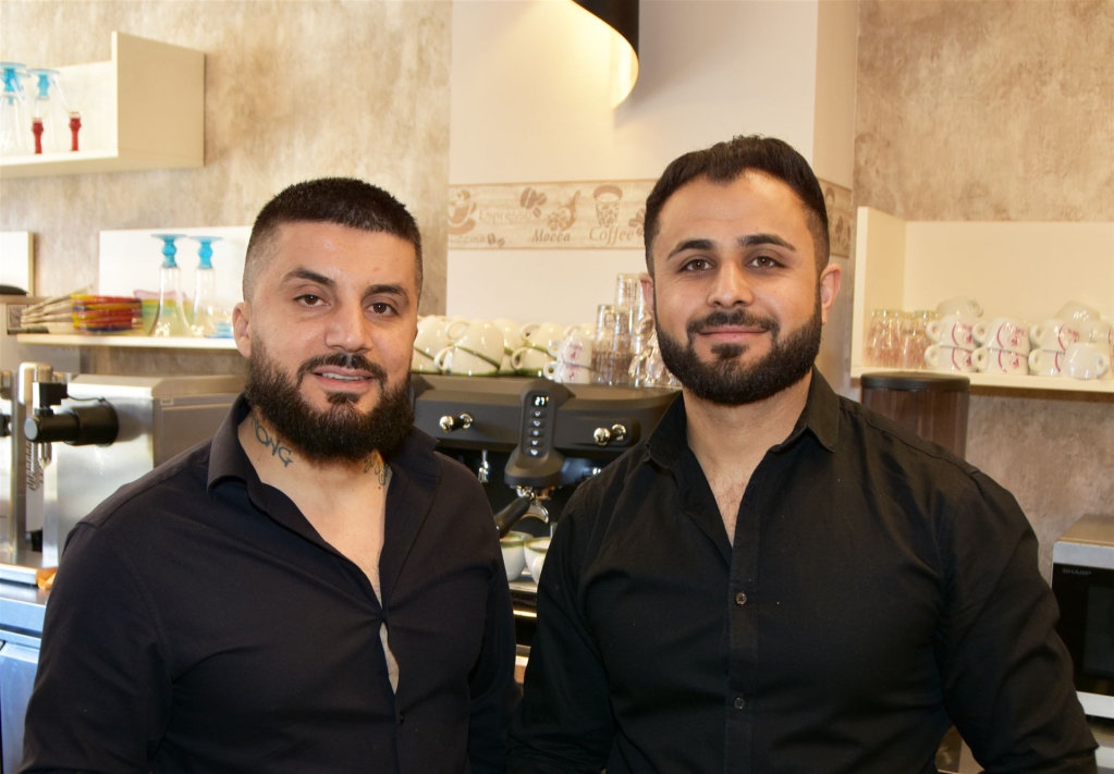 Zwei Männer stehen in einer modernen, hellen Kaffeerösterei und lächeln in die Kamera.
